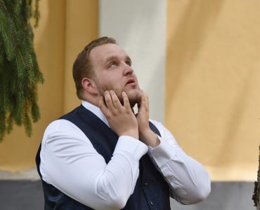 A man in formal attire looks contemplative under trees in Vásárosnamény.