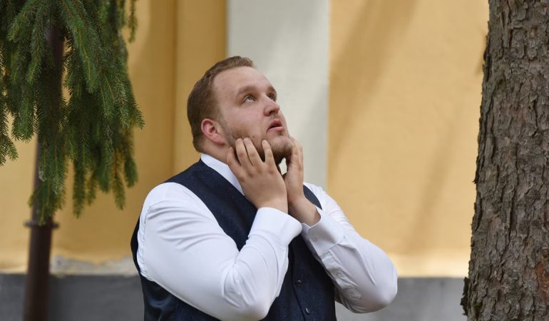 A man in formal attire looks contemplative under trees in Vásárosnamény.