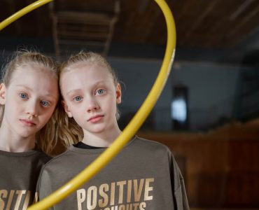 Twin girls in sportswear indoors with a hula hoop expressing positivity. Perfect for family and sports themes.